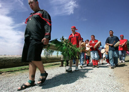 Group of Indigenous people carrying salmon on a cedar plank as part of a traditional Tulalip ceremony.