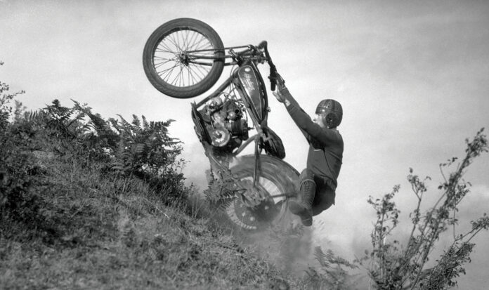 A person riding a motorcycle up a steep hill with only the rear wheel on the ground.