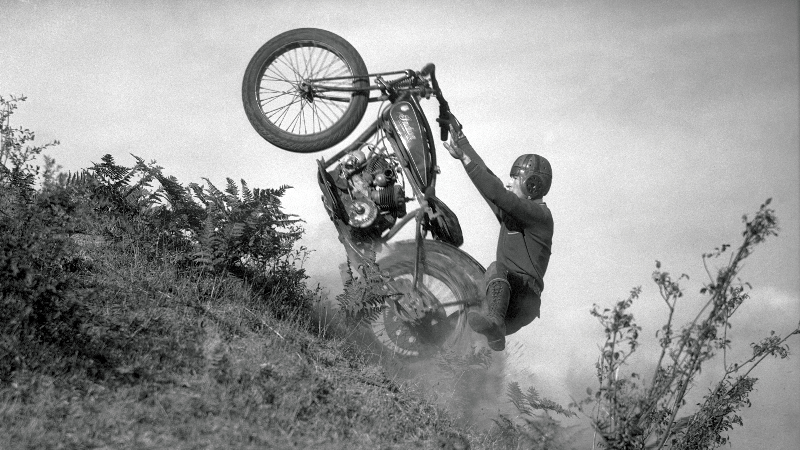 A person riding a motorcycle up a steep hill with only the rear wheel on the ground.