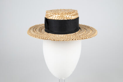 A woven straw hat with a flat brim and black ribbon tied around the base.