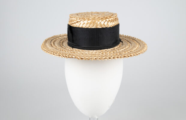 A woven straw hat with a flat brim and black ribbon tied around the base.