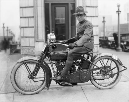 Seattle police officers lined up on motorcycles along Fourth Avenue, circa 1915. The officers wear dark uniforms and caps, standing beside early model motorcycles in front of a downtown storefront.