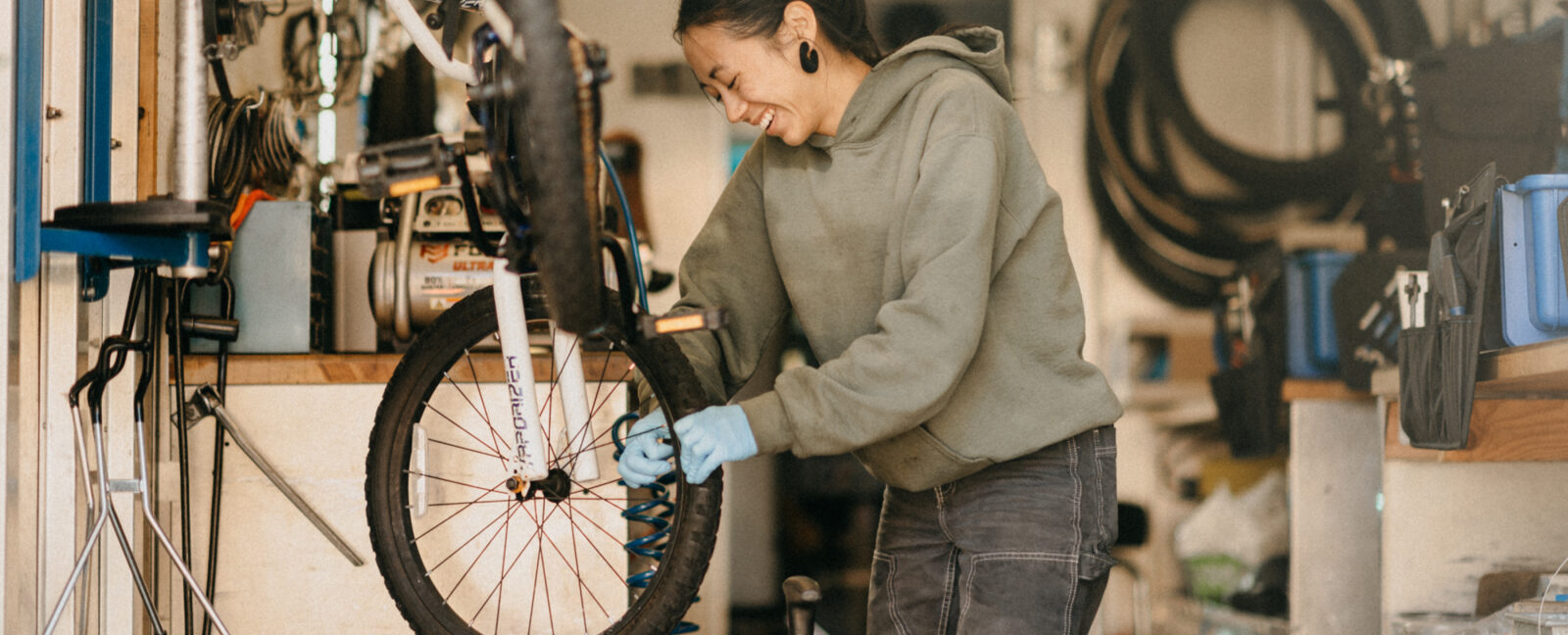 A bicycle technician in a bike repair shop works on the front tire of an elevated bicycle.