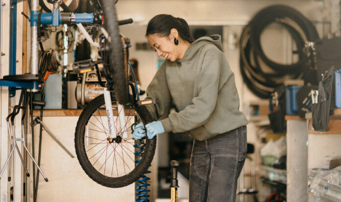 A bicycle technician in a bike repair shop works on the front tire of an elevated bicycle.