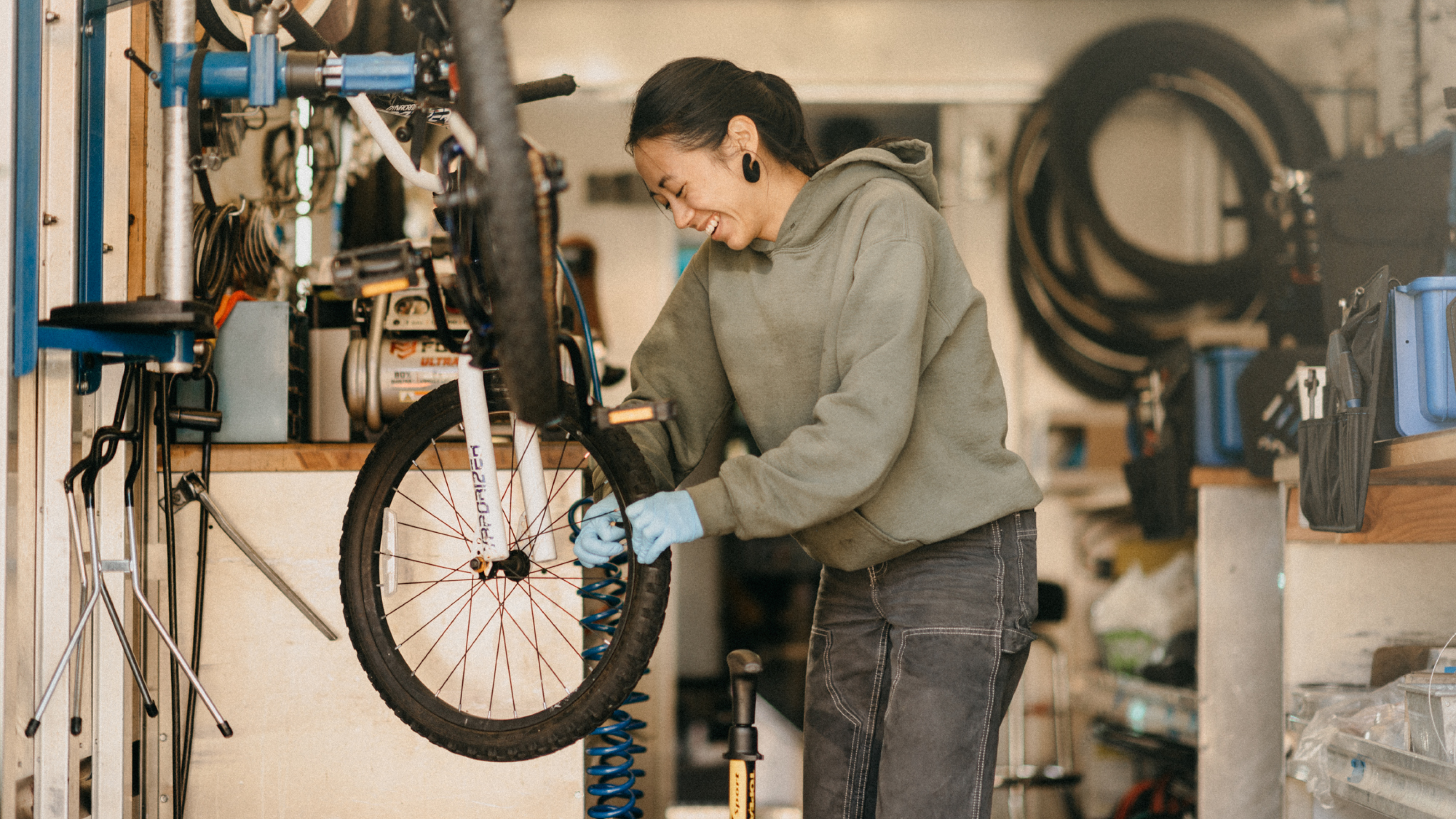 A bicycle technician in a bike repair shop works on the front tire of an elevated bicycle.