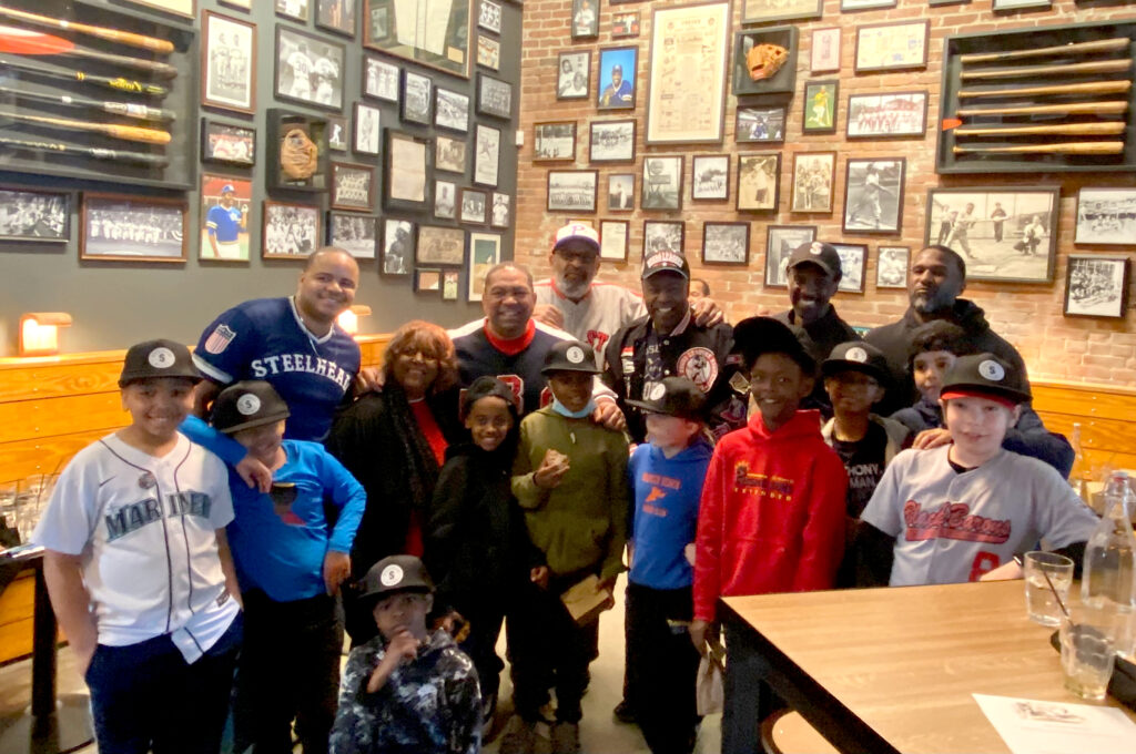 Rising Sons Extended leaders and members in restaurant posing before a wall full of baseball memorabilia.