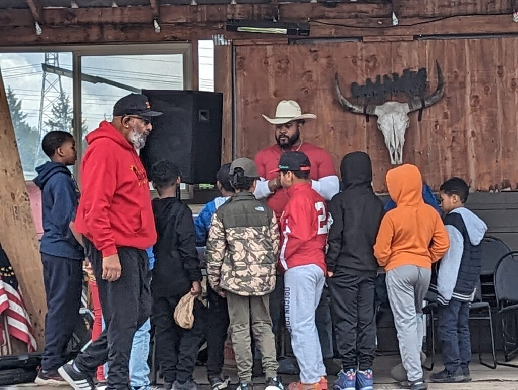 Rising Sons Extended members on field trip to farm listen to presentation from man in a cowboy hat.