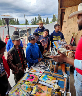 Rising Sons Extended members on field trip to farm listen to presentation from man in a cowboy hat.