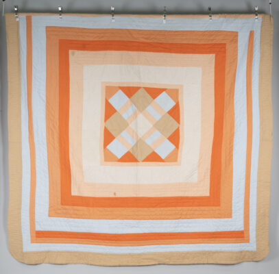 Handmade quilt with striped borders of dark orange, light orange, and white fabric and an offset checkered pattern in the middle.