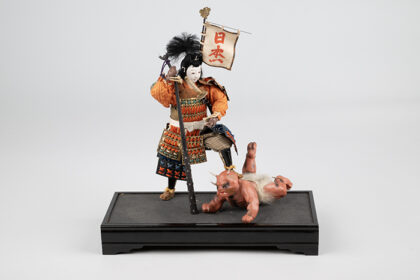 Boys' Day doll figure of Momotarō, the Peach Boy hero from Japanese folklore, in samurai armor standing over a red ogre; part of MOHAI's collection representing Japanese cultural heritage during WWII.