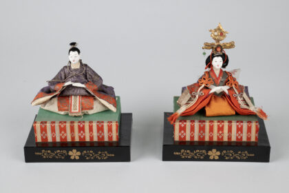 Emperor and Empress dolls from a Japanese Girls' Day set, dressed in ornate purple and red court garments and displayed on tiered platforms; part of MOHAI's Japanese American doll collection.