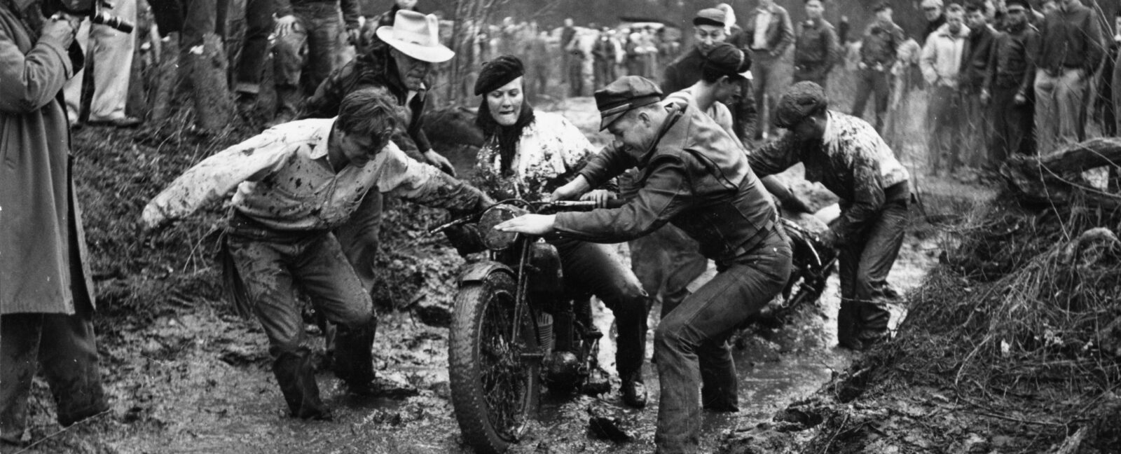 A group of volunteers assist motorcycle rider Donna Walters in the 1953 Queen City Mud Run.