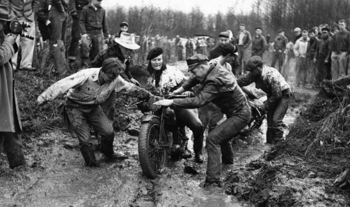 A group of volunteers assist motorcycle rider Donna Walters in the 1953 Queen City Mud Run.