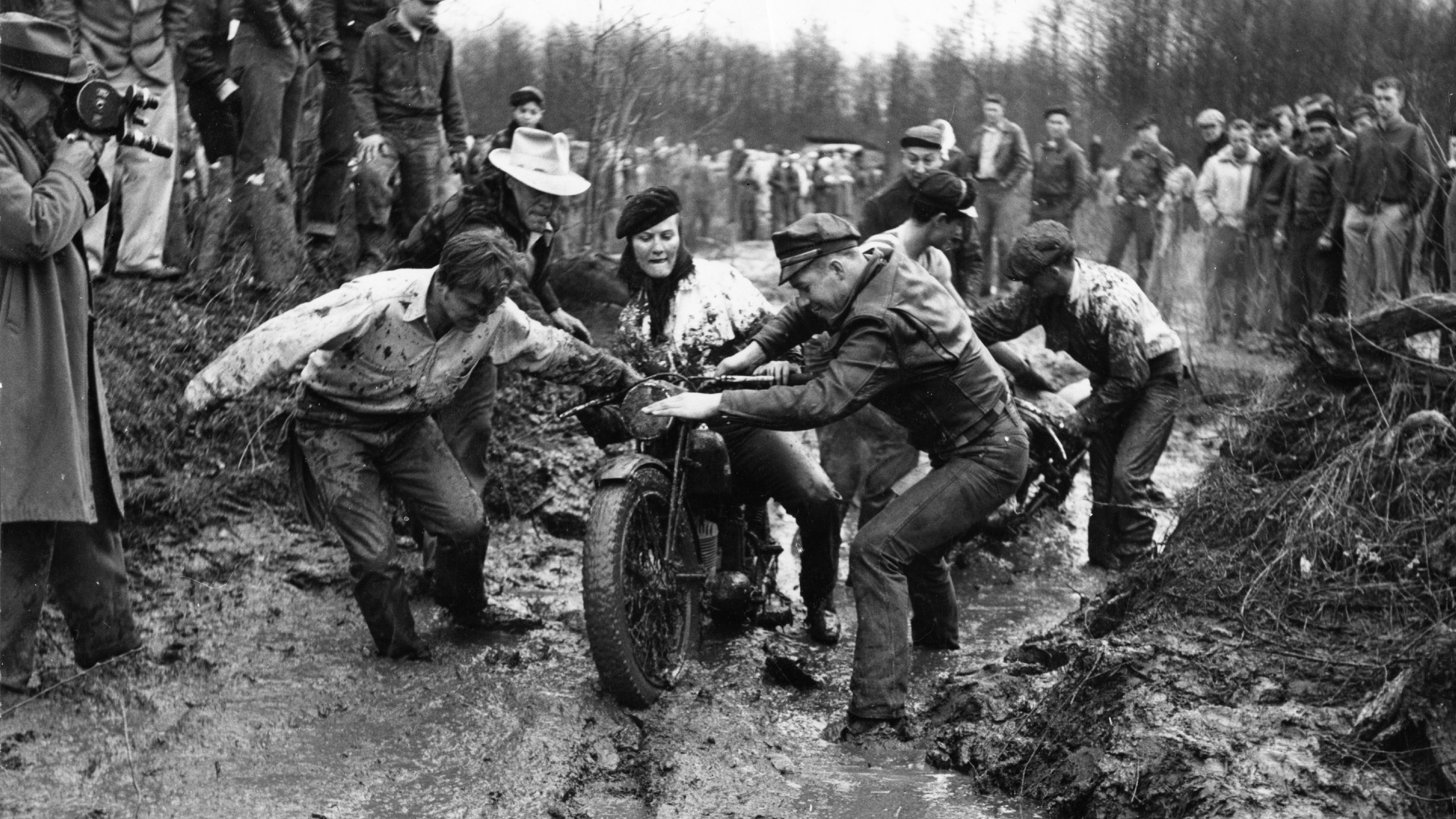 A group of volunteers assist motorcycle rider Donna Walters in the 1953 Queen City Mud Run.
