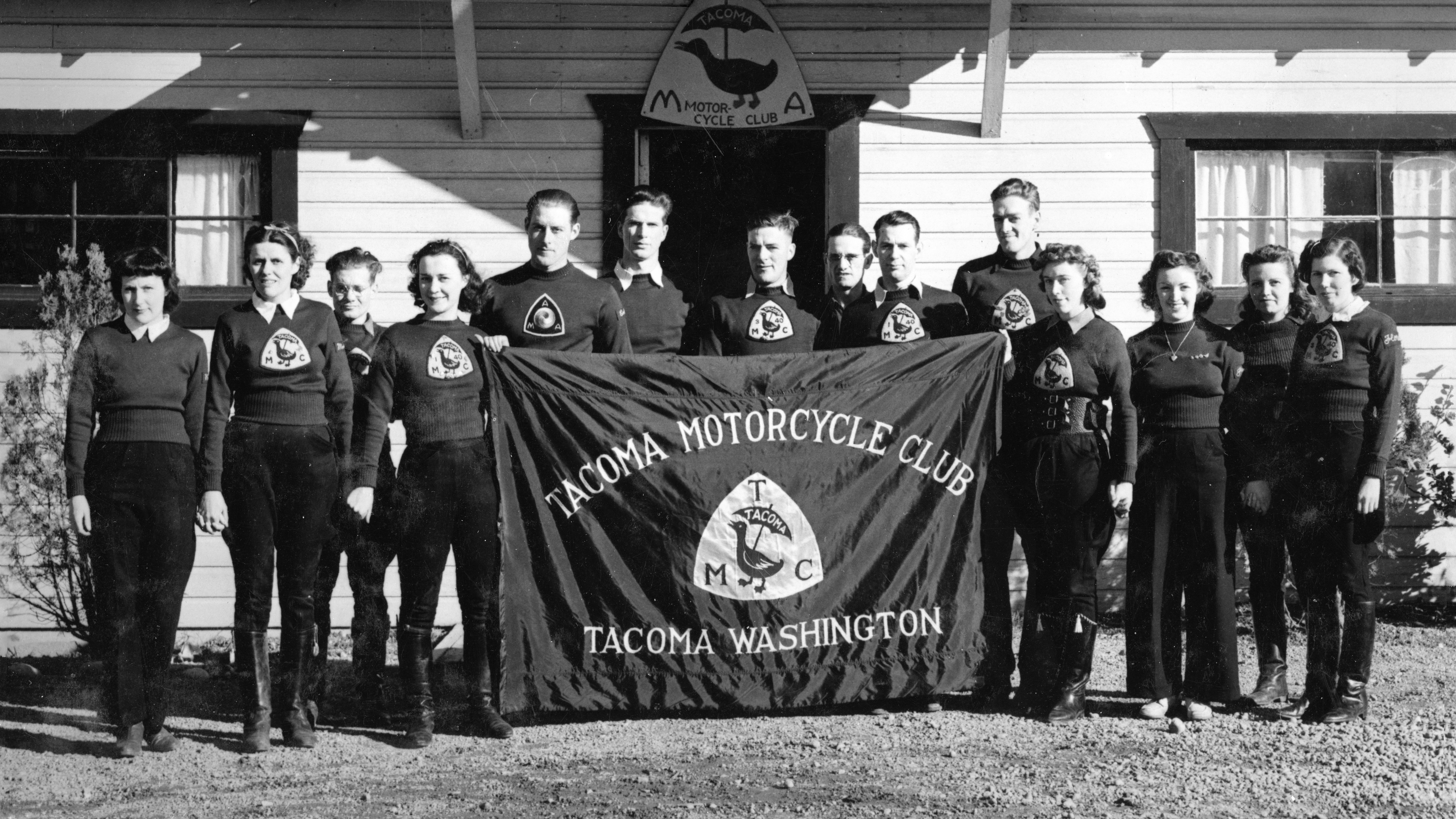 Fourteen male and female members of the Tacoma Motorcycle Club with a team banner in 1937.