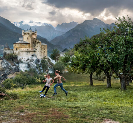 Kids playing soccer in an orchard with a castle in the background.